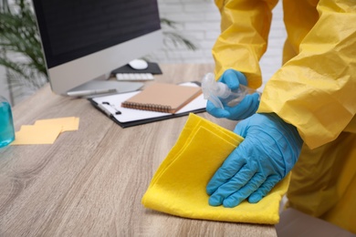 Janitor in protective suit disinfecting office furniture to prevent spreading of COVID-19, closeup