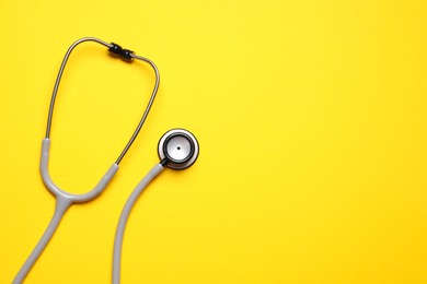 Stethoscope on yellow background, top view. Space for text