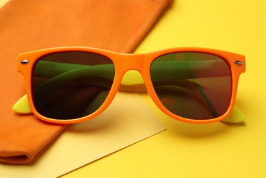 Stylish sunglasses with bag on yellow background, closeup