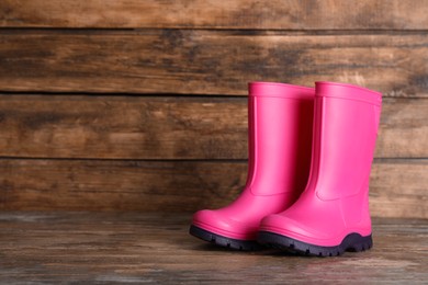 Pair of bright pink rubber boots on wooden surface. Space for text