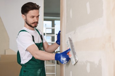 Photo of Worker in uniform plastering wall with putty knife indoors. Space for text