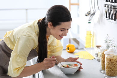 Young woman eating tasty vegetable soup at countertop in kitchen