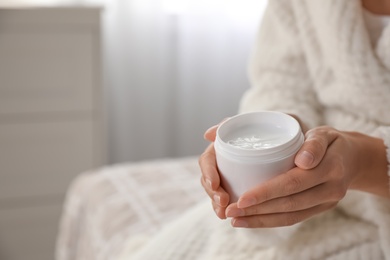 Woman with jar of moisturizing cream indoors, closeup