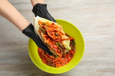 Photo of Woman preparing spicy cabbage kimchi at wooden table, top view