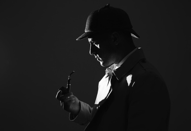 Old fashioned detective with smoking pipe on dark background, black and white effect