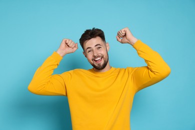 Excited man in yellow sweatshirt celebrating victory on light blue background