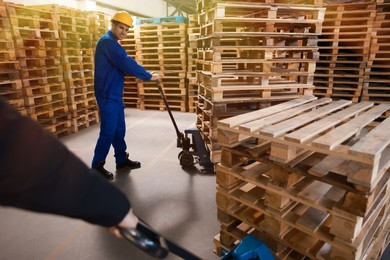 Workers moving wooden pallets with manual forklift in warehouse