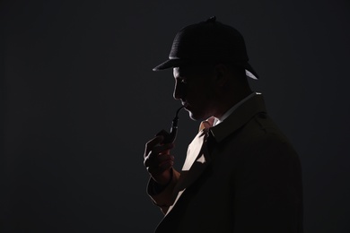 Old fashioned detective with smoking pipe on dark background. Space for text