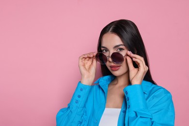 Attractive serious woman wearing fashionable sunglasses against pink background. Space for text