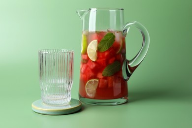 Photo of Tasty summer watermelon drink with lime in glass jug on pale light green background