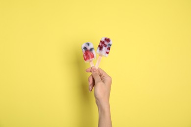 Woman holding berry popsicle on yellow background, closeup