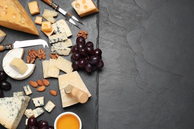 Cheese platter with specialized knife and fork on black table, flat lay .Space for text