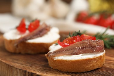 Photo of Delicious sandwiches with cream cheese, anchovies and tomatoes on wooden board, closeup. Space for text