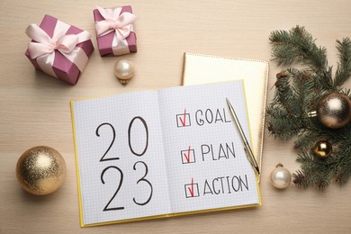 Flat lay composition of notebook with text 2023 Goal, Plan, Action and festive decor on wooden table. New Year resolutions