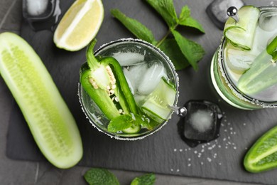 Photo of Spicy cocktail with jalapeno, cucumber and lime on black table, flat lay