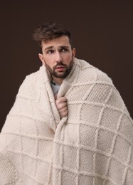 Man wrapped in blanket suffering from fever on brown background. Cold symptoms