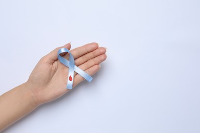 Woman holding light blue ribbon with drop of blood on white background, top view. Diabetes awareness