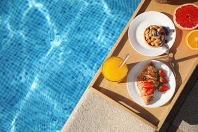 Tray with delicious breakfast near swimming pool, top view. Space for text