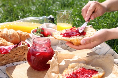 Woman spreading jam on croissant outdoors, closeup. Summer picnic