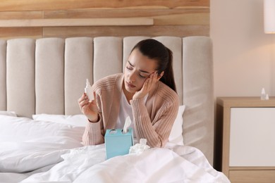 Sick young woman with napkins and nasal spray in bed at home