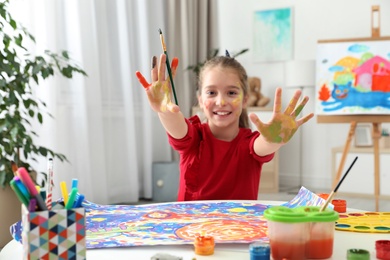Little child with painted hands and face at table indoors