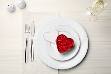 Photo of Beautiful table setting. Dishware and decorative heart shaped box with roses for romantic dinner on white wooden table, flat lay