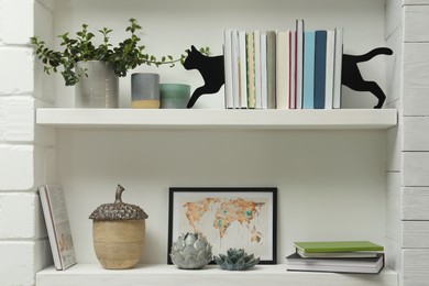 Cat shaped bookends with books and different decor on shelves indoors. Interior design