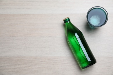 Glass and bottle with water on wooden background, flat lay. Space for text
