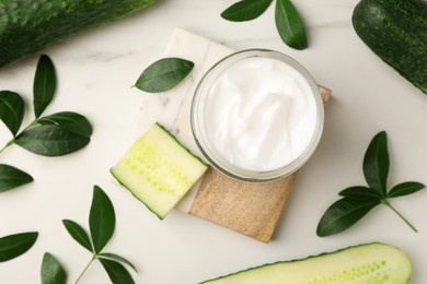 Glass jar of cucumber face cream on white marble table, flat lay