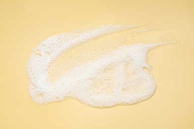Photo of Smudge of white washing foam on yellow background, top view