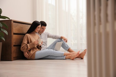 Happy couple with laptop sitting on warm floor at home. Heating system