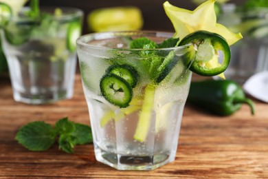 Photo of Spicy cocktail with jalapeno, carambola and mint on wooden table, closeup