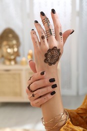 Woman with henna tattoo on hand indoors, closeup. Traditional mehndi ornament