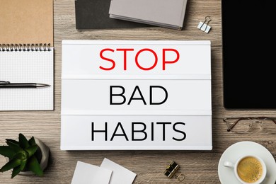 Lightbox with phrase Stop Bad Habits, cup of coffee and stationery on wooden table, flat lay