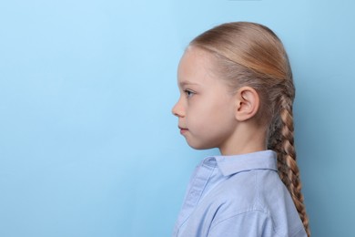 Profile portrait of cute little girl on light blue background. Space for text