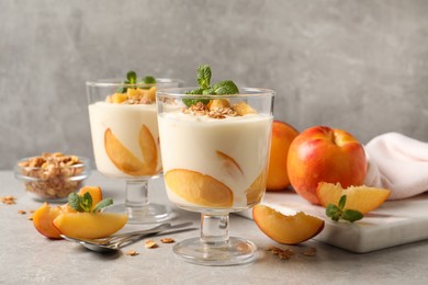 Tasty peach yogurt with granola, mint and pieces of fruits on light grey table