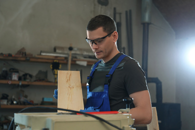 Professional carpenter with wooden board in workshop