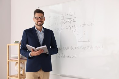 Photo of Happy teacher with book at whiteboard in classroom during math lesson