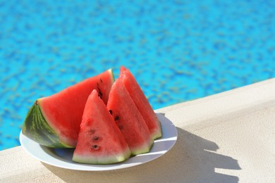 Slices of watermelon on white plate near swimming pool outdoors. Space for text