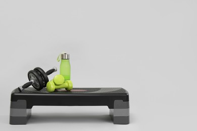 Step platform, water bottle, dumbbells and abdominal wheel on light background, space for text. Sport equipment