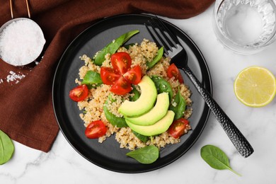 Photo of Delicious quinoa salad with tomatoes, avocado slices and spinach leaves served on white marble table, flat lay