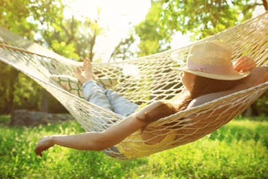 Photo of Young woman with hat resting in comfortable hammock at green garden