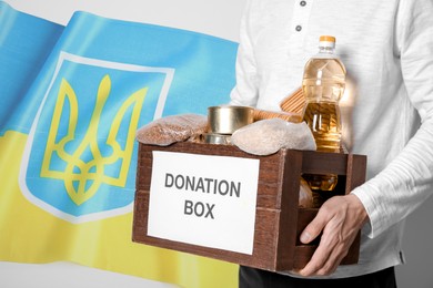 Volunteer holding donation box with Ukrainian flag on background. Help during war