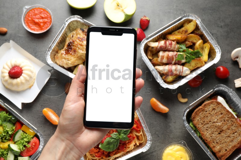 Top view of woman holding smartphone over grey table with lunchboxes, mockup for design. Healthy food delivery
