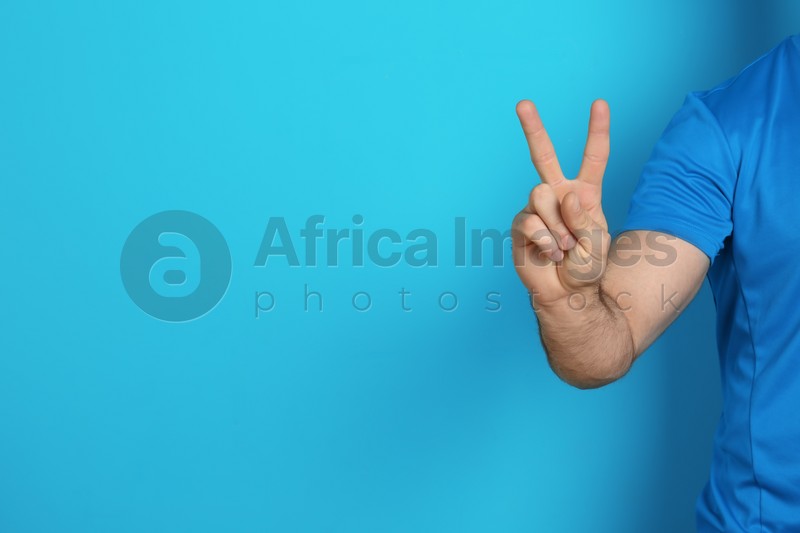 Photo of Young man showing victory gesture on color background. Space for text