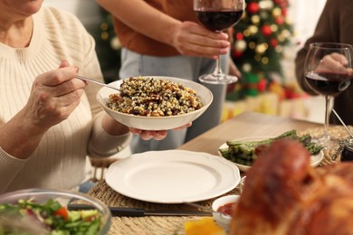 Woman with bowl of traditional Christmas kutia and her family at festive dinner, closeup. Slavic dish