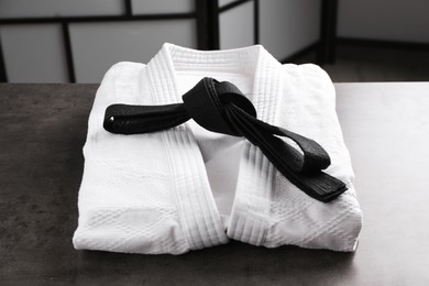 Martial arts uniform with black belt on grey stone table indoors