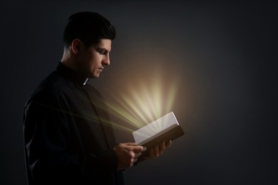 Priest holding Bible with holy light on black background