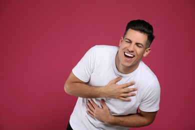 Handsome man laughing on maroon background. Funny joke