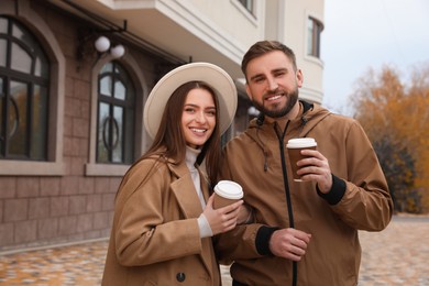 Happy couple wearing stylish autumn clothes with cups of coffee on city street
